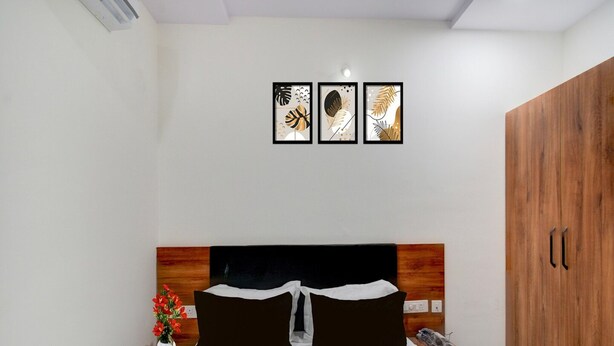 Une chambre à coucher comprenant un lit, une tête de lit en bois, des tables de chevet, une armoire en bois et trois œuvres d’art encadrées accrochées au mur.