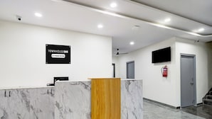 Un comptoir d’accueil avec un plateau en marbre et un panneau en bois, une pancarte indiquant qu’il est entretenu par l’entreprise, un extincteur et un escalier en arrière-plan.