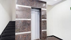 Un intérieur moderne avec un escalier, une porte ornée d’un mur en marbre et un mur blanc sobre agrémenté d’une enseigne verte.