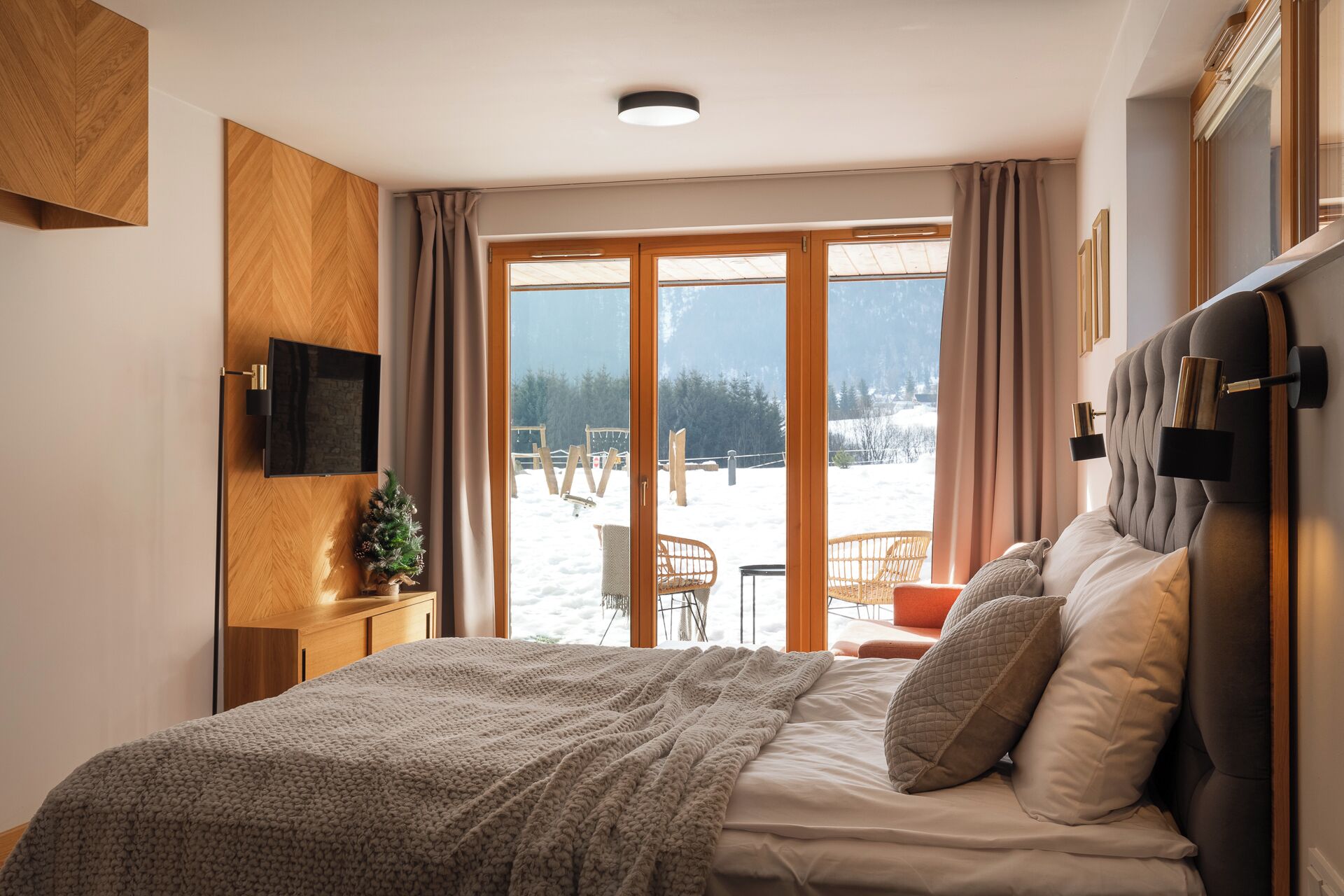 Une chambre avec un grand lit, un téléviseur fixé au mur et une vue sur un espace extérieur enneigé.
