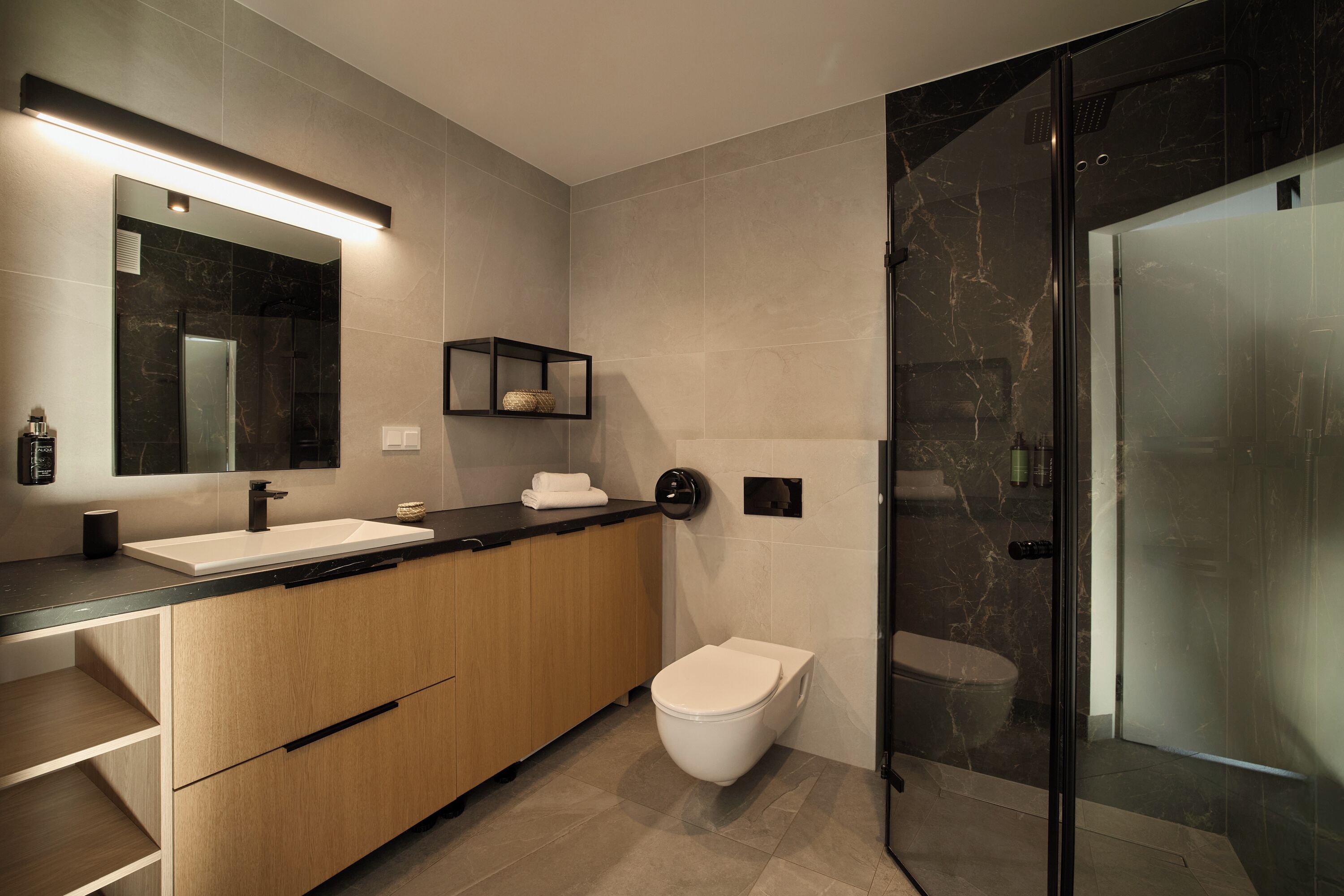 Un baño moderno con un espejo grande, un lavamanos, un inodoro y una ducha con mampara de vidrio.