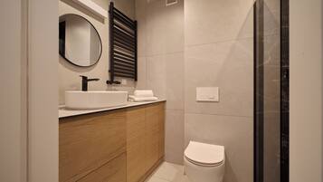 Une salle de bain moderne avec un meuble-lavabo en bois, un miroir rond, un lavabo blanc, des toilettes et un espace douche.