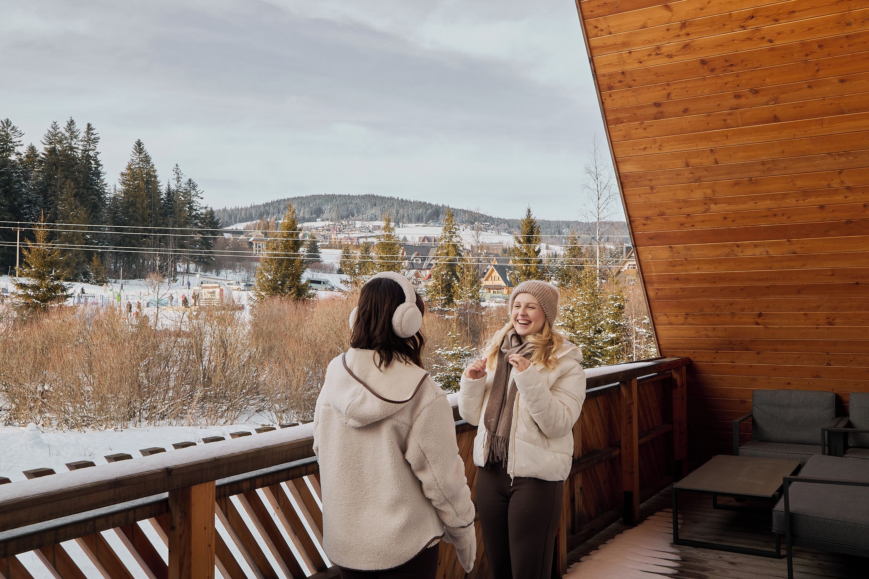 Une terrasse en bois offrant une vue sur un paysage enneigé et sur une ville située au loin.