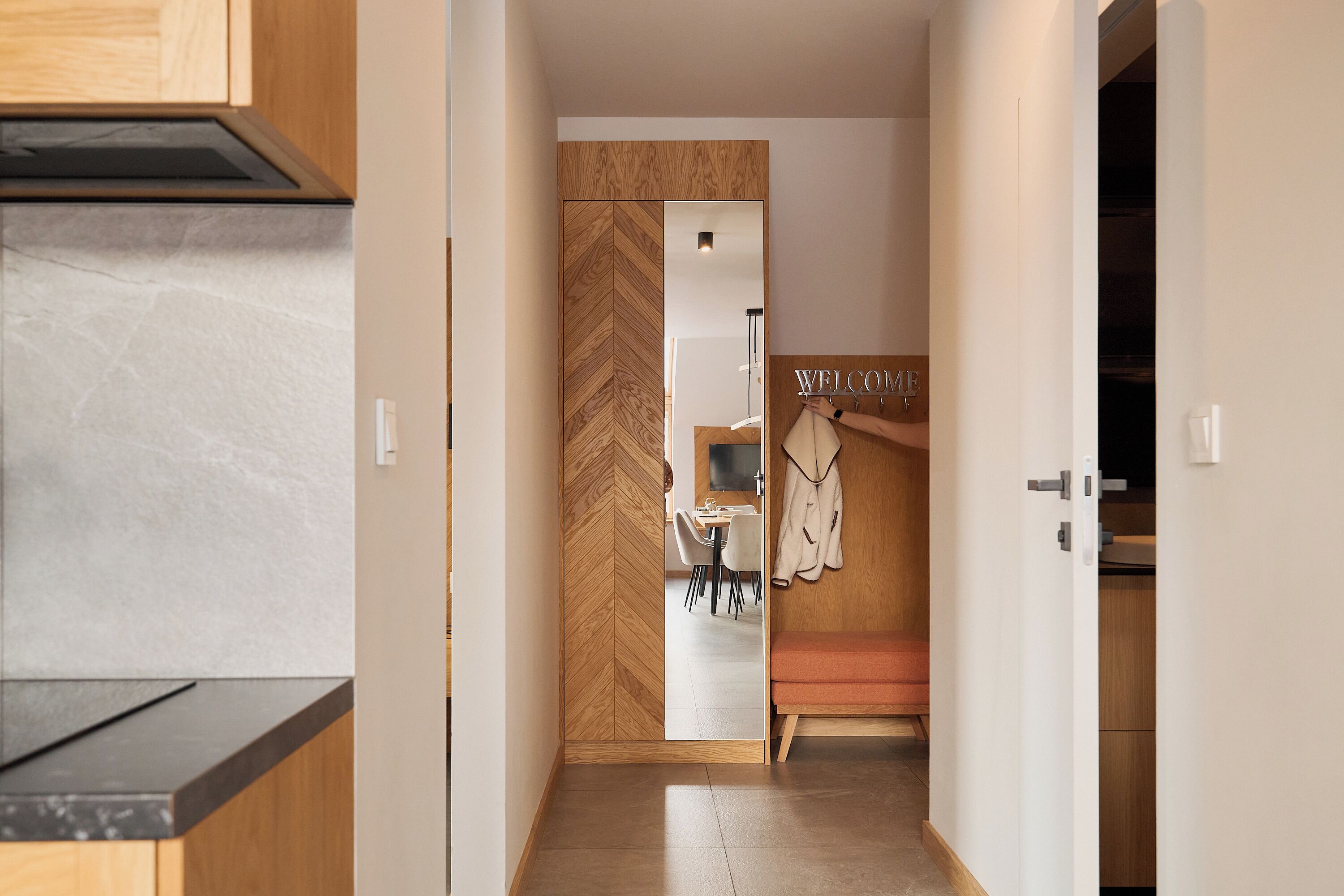 Cozinha moderna com porta em padrão herringbone que dá para uma sala de jantar com um letreiro 'WELCOME'.