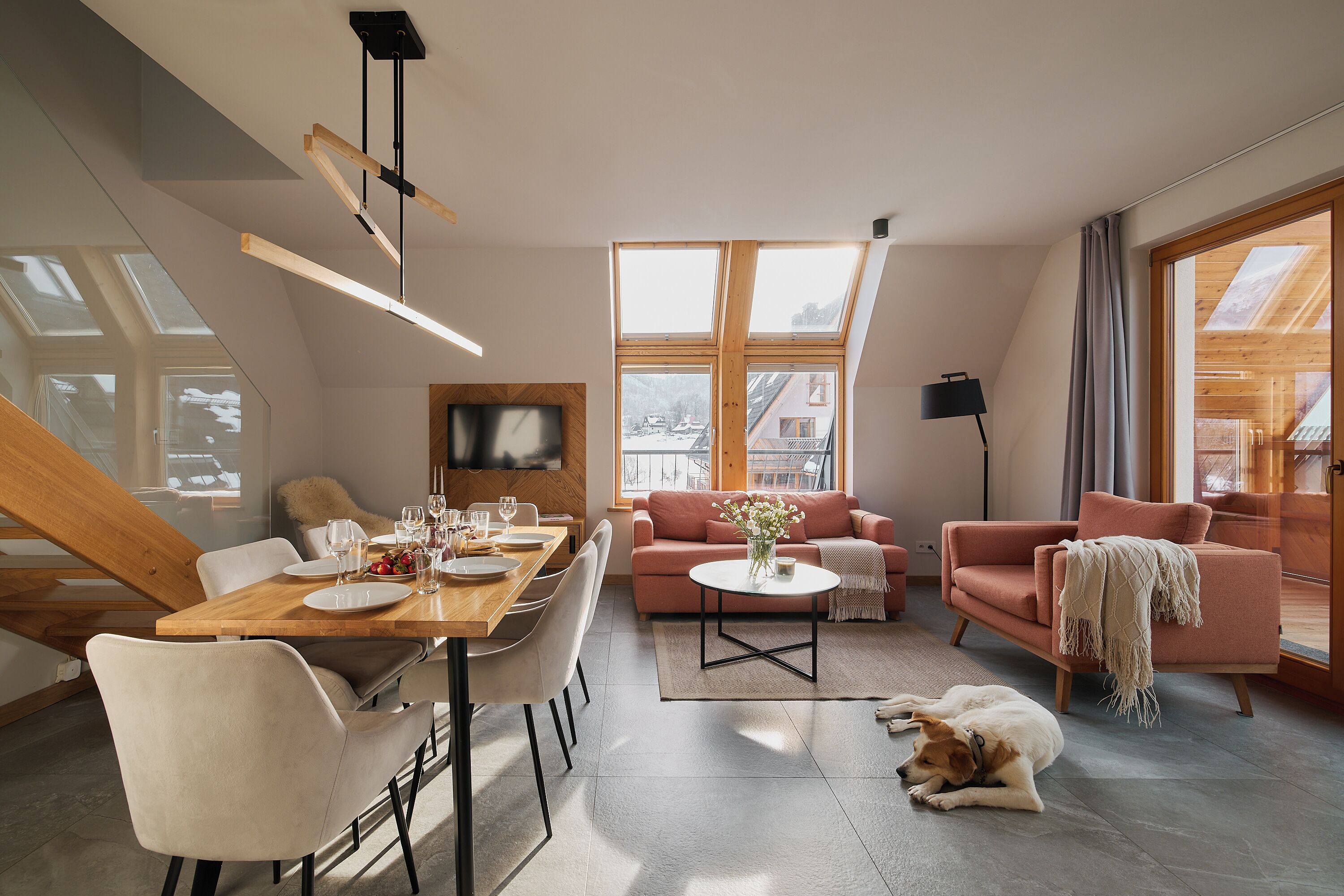 Un salon moderne avec un coin repas, de grandes fenêtres et un chien qui se repose sur le sol.