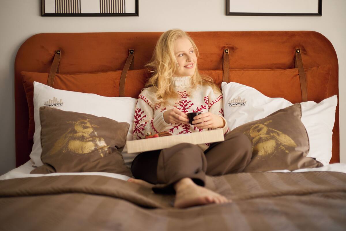 Une personne assise sur un lit dont la tête de lit est marron, tenant un livre.