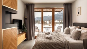 Une chambre moderne avec un lit, une télévision et une vue sur les montagnes grâce à de grandes fenêtres.