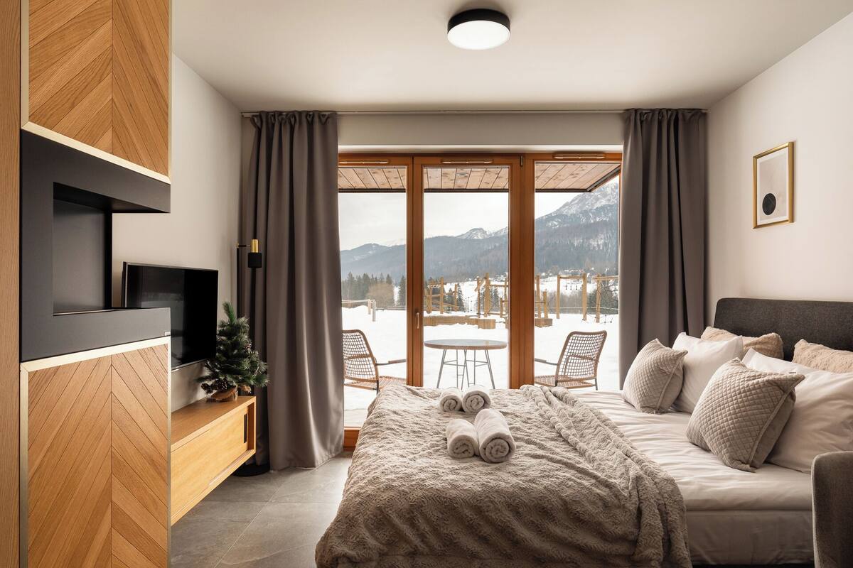 Une chambre moderne avec un lit, une télévision et une vue sur les montagnes grâce à de grandes fenêtres.