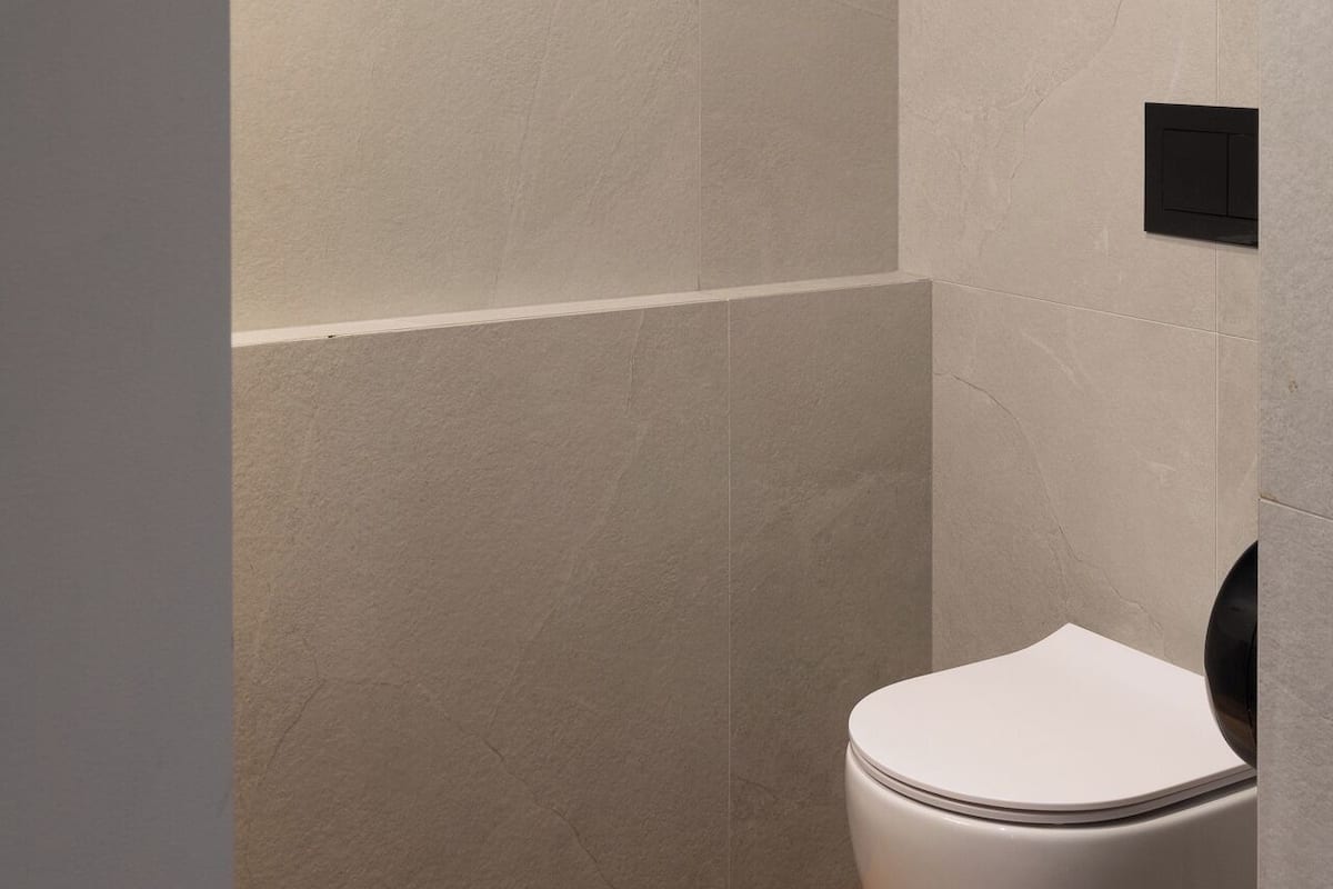 Een badkamer met een wit toilet, een houten vloer en beige betegelde muren.