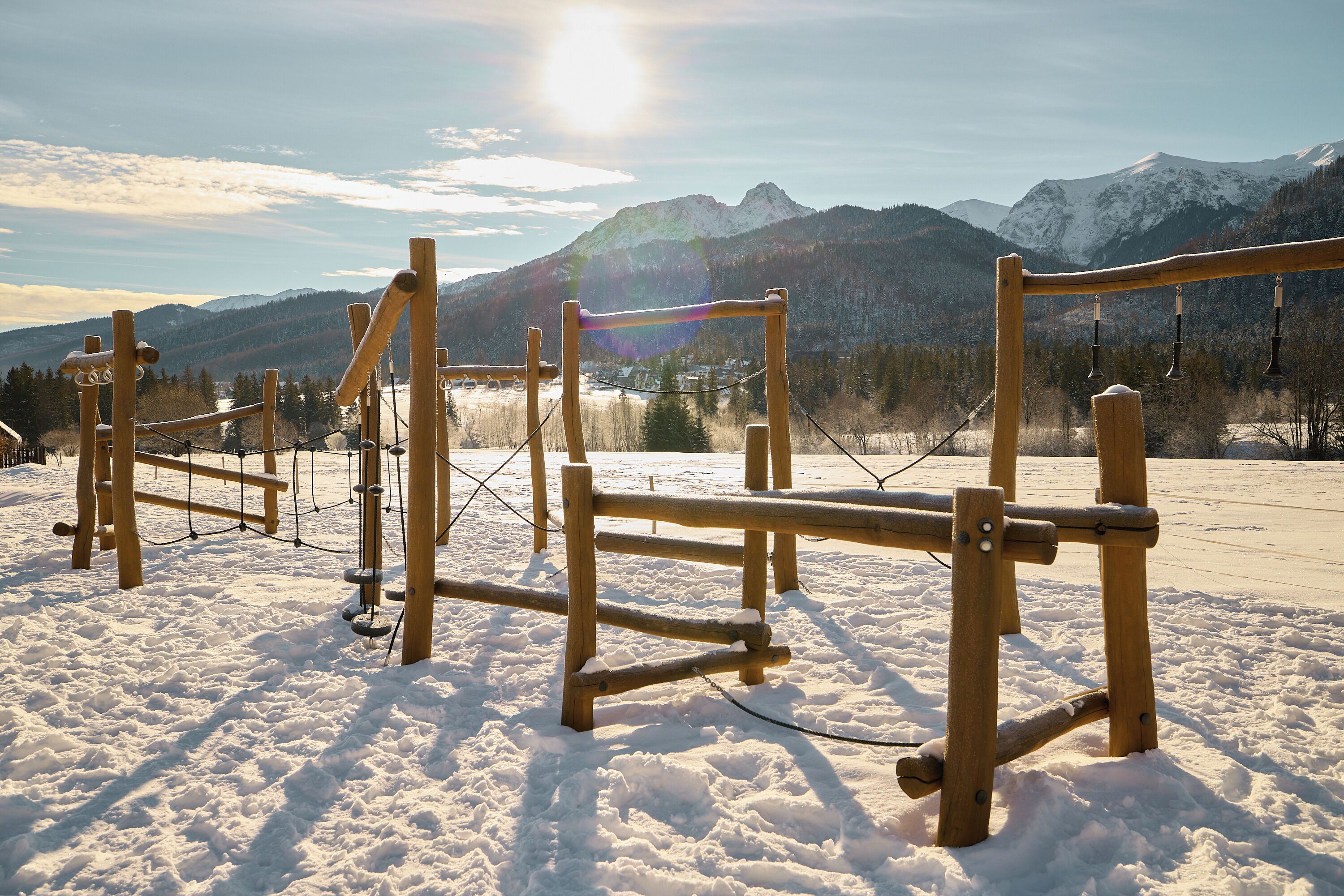 A wooden climbing structure in a snowy landscape with mountains in the background.