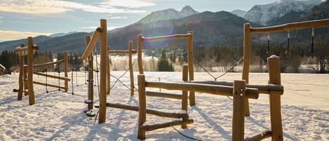 A wooden climbing structure in a snowy landscape with mountains in the background.