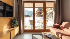 Un salon confortable avec une grande télévision, un meuble en bois et un canapé. Il est doté d’une porte-fenêtre coulissante qui donne sur un espace extérieur avec une terrasse en bois et un bonhomme de neige.