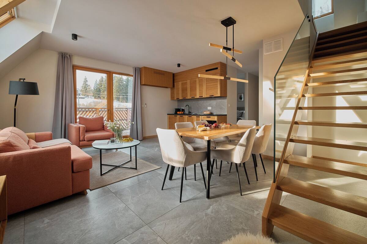 Un salon moderne avec un canapé, une table basse et un coin repas. Un escalier mène à l’étage supérieur.