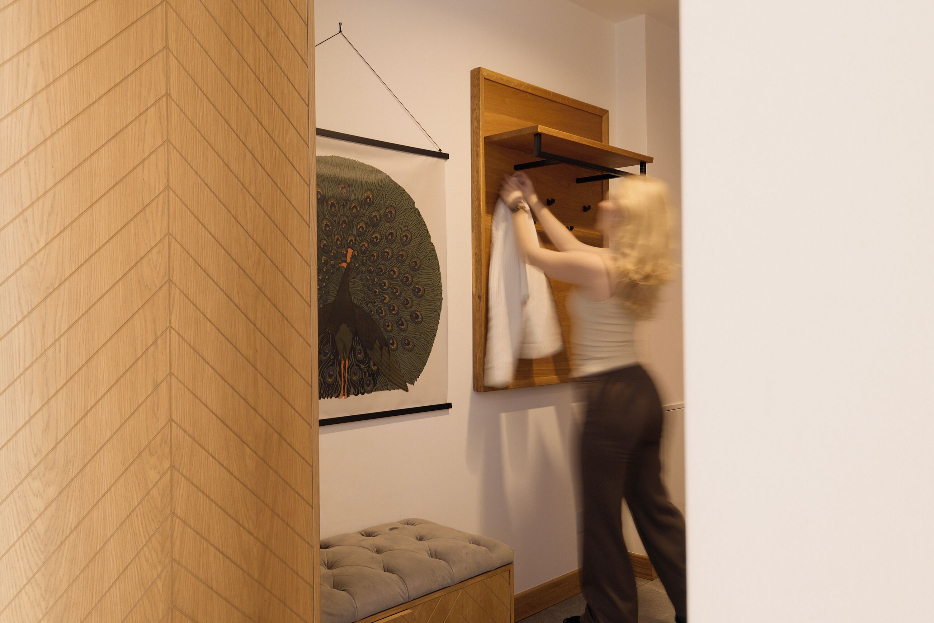 A room with a wooden floor, a bench, a wall-mounted artwork, and a clothing rack.