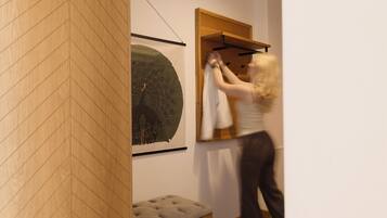 A room with a wooden floor, a bench, a wall-mounted artwork, and a clothing rack.