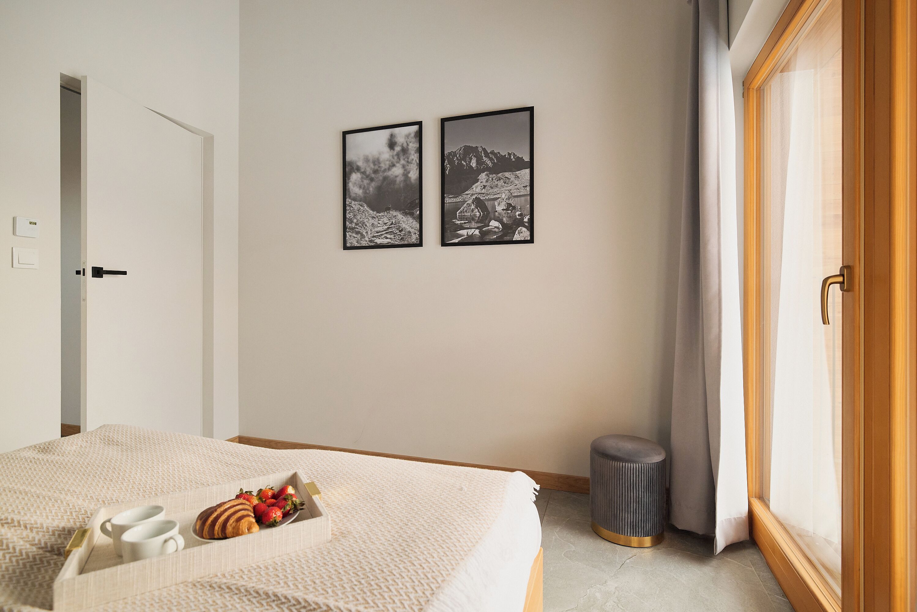A neatly arranged bedroom with a bed, breakfast tray, two framed pictures, and a small trash bin.
