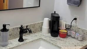 A bathroom with a granite countertop, a sink, a coffee maker, and a mirror.