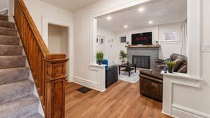 A modern living room with a fireplace, a TV mounted above it, and a staircase leading to another level. - Minutes to Hospital, Cozy 3BR w/ Game Room, Family-Friendly (Columbus)
