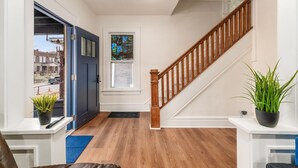 A hallway with a wooden staircase, a blue door, and a window with a stained glass view. - Minutes to Hospital, Cozy 3BR w/ Game Room, Family-Friendly (Columbus)