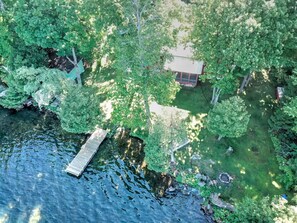 An aerial view of a lakeside property with a dock, a small cabin, and dense surrounding trees. - Belsize Cottage, Upper Rideau Lake (Portland)