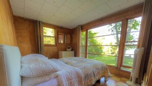 Een slaapkamer met een bed, nachtkastje, spiegel en raam met uitzicht op groen.