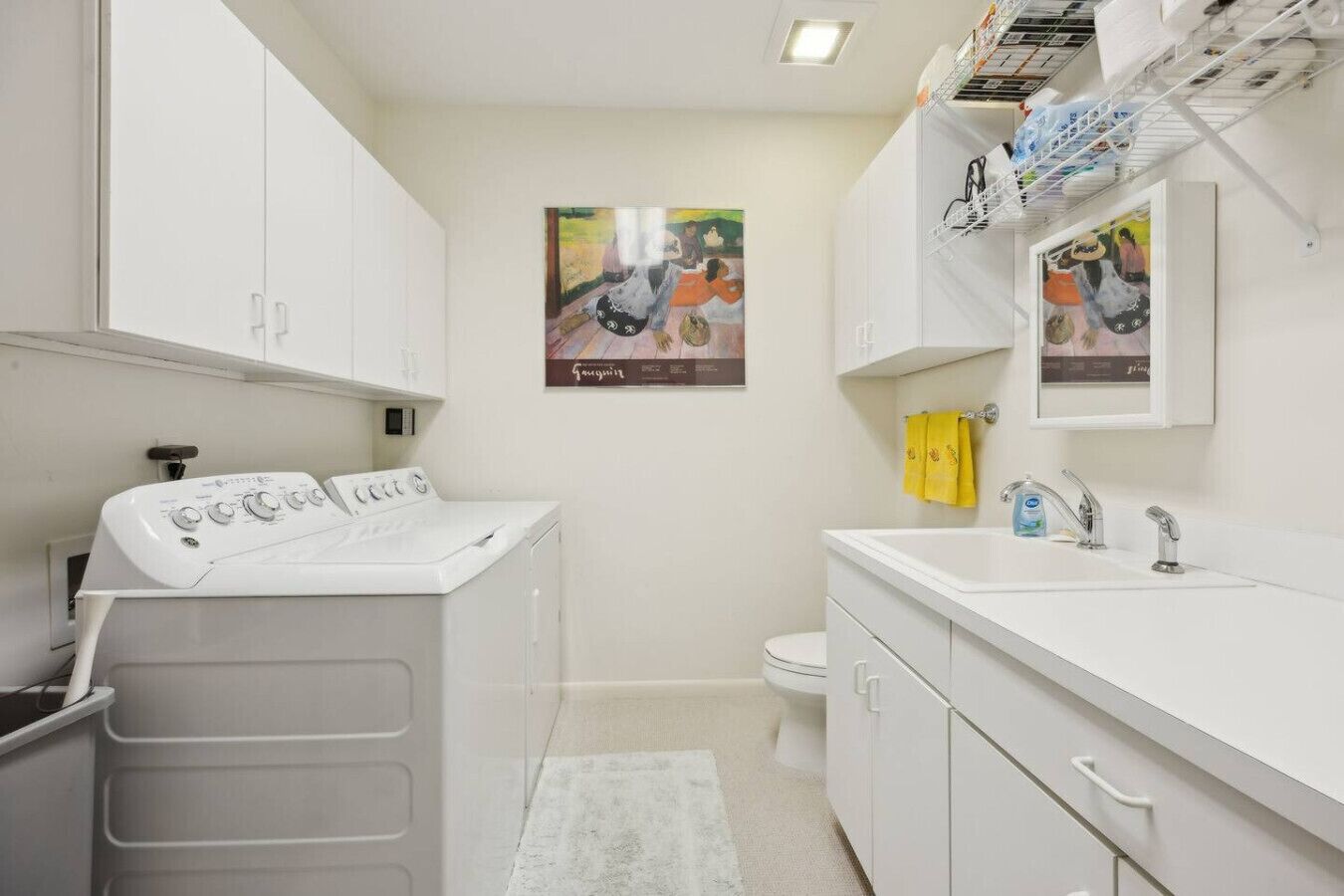 Een moderne badkamer met een voorlader wasmachine, een wastafel met spiegel en twee ingelijste kunstwerken aan de muur.
