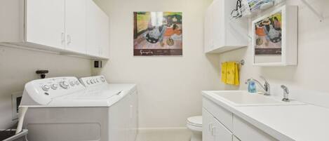 Een moderne badkamer met een voorlader wasmachine, een wastafel met spiegel en twee ingelijste kunstwerken aan de muur.