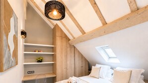 Ein Schlafzimmer mit geneigter Decke, einem Dachfenster, einem Bett mit weißer Bettwäsche, einem Nachttisch und einer Wandablage mit Dekoration.