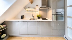 Eine moderne Küche mit schrägverdeckter Decke, eingebauten Schränken, einer Edelstahl-Spüle und einer Dunstabzugshaube.