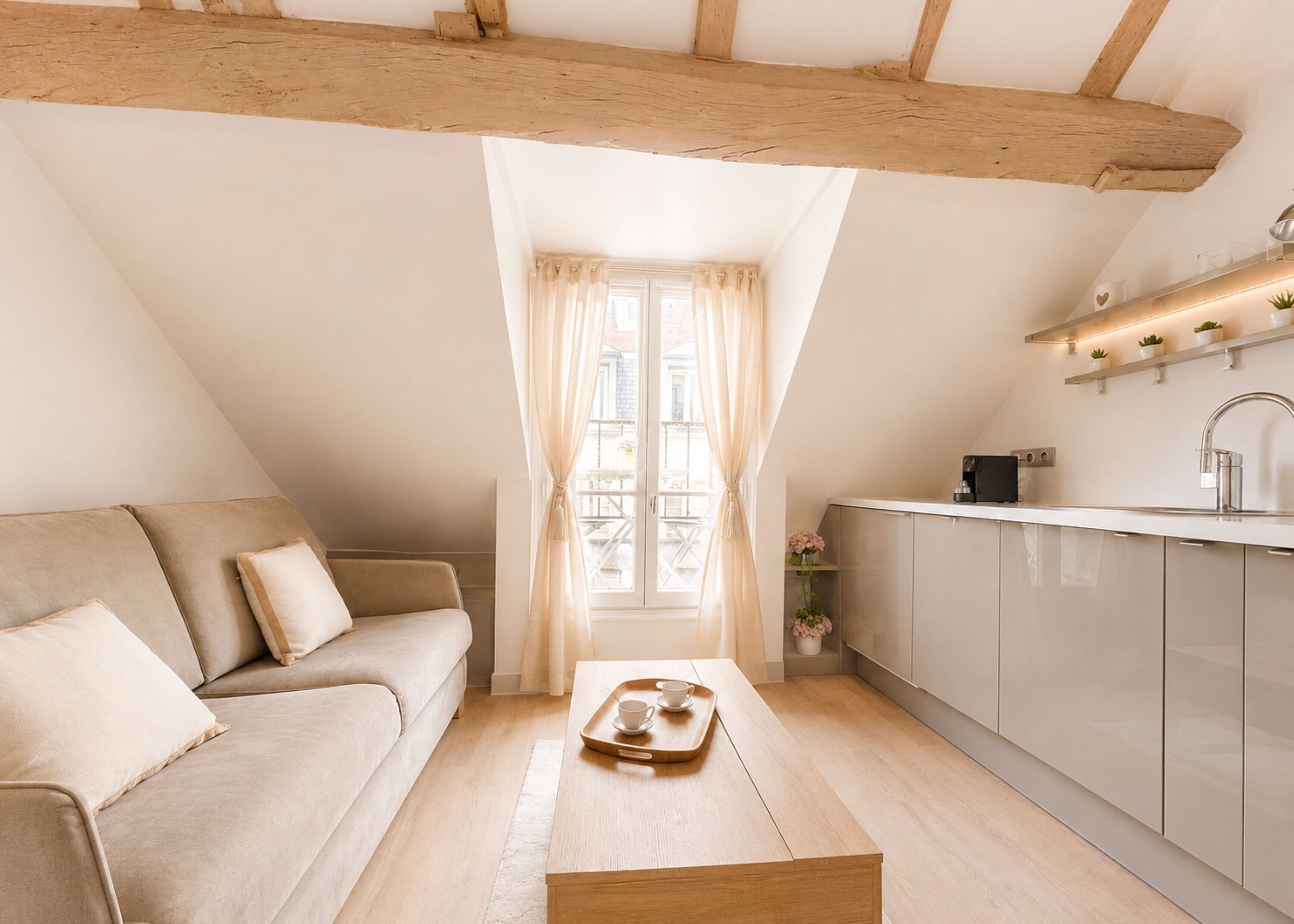 Un dormitorio tipo loft acogedor, con techo inclinado, un ventanal con cortinas, una cama y una pequeña kitchenette.