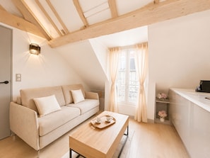 A cozy loft bedroom with a wooden ceiling, a sofa, a dining table, and a kitchen area. - 1531 Bourgeois (Paris)