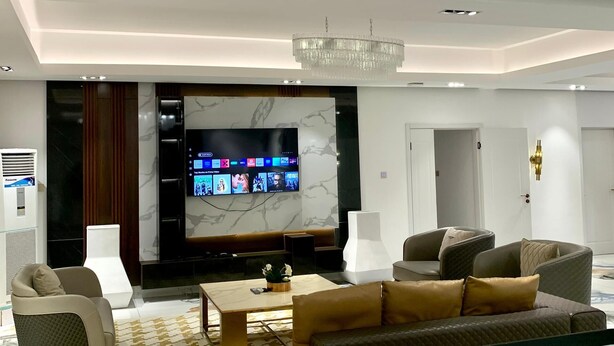 Un salon moderne doté d’un grand téléviseur à écran plat, de sièges confortables, d’un lustre et d’un mur décoratif en marbre.