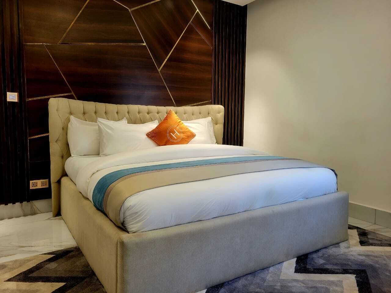 A large bed with a tufted headboard, white and blue bedding, and a single orange accent pillow.