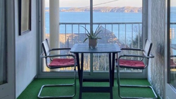 Un balcon avec une table et deux chaises, un pot de fleurs et une vue sur un pont et des montagnes.