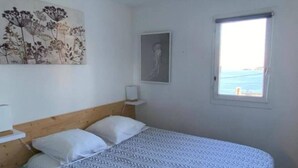 Une chambre à coucher comprenant un lit, une table de chevet, une commode, une fenêtre donnant sur un paysage agréable et un mur orné d’un tableau représentant des motifs floraux.
