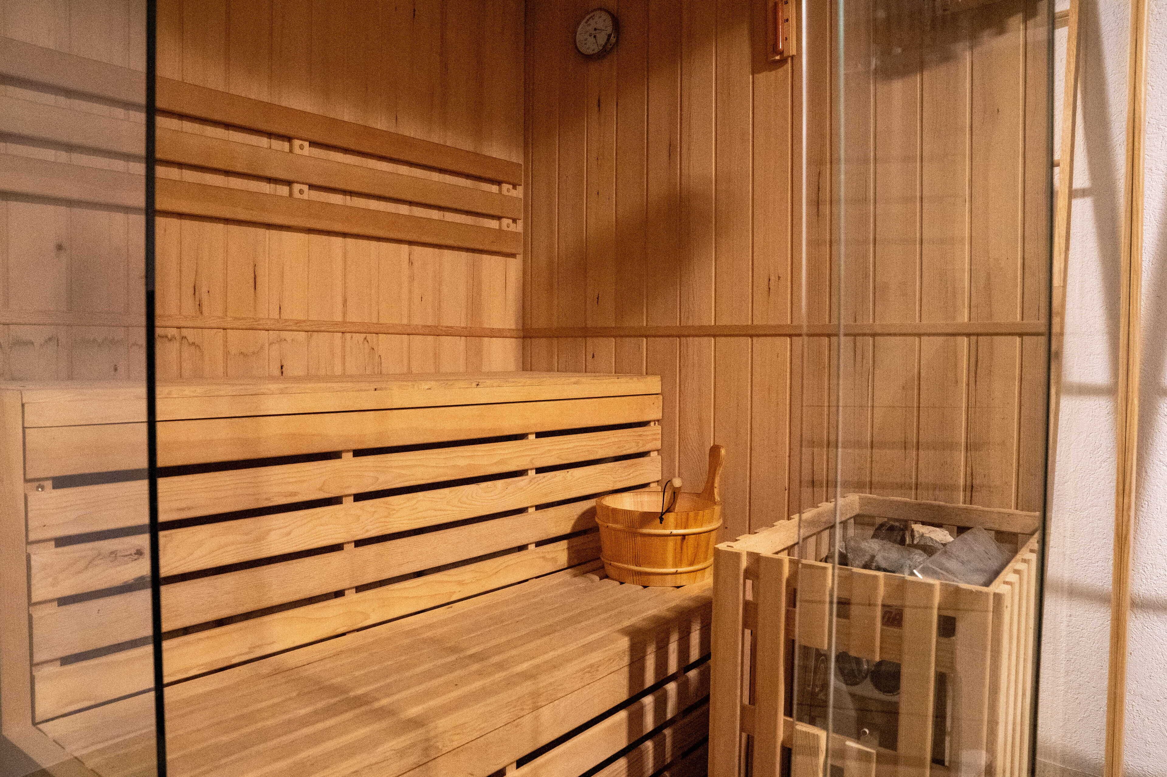 A wooden sauna bench with a wooden bucket and a glass container with stones.