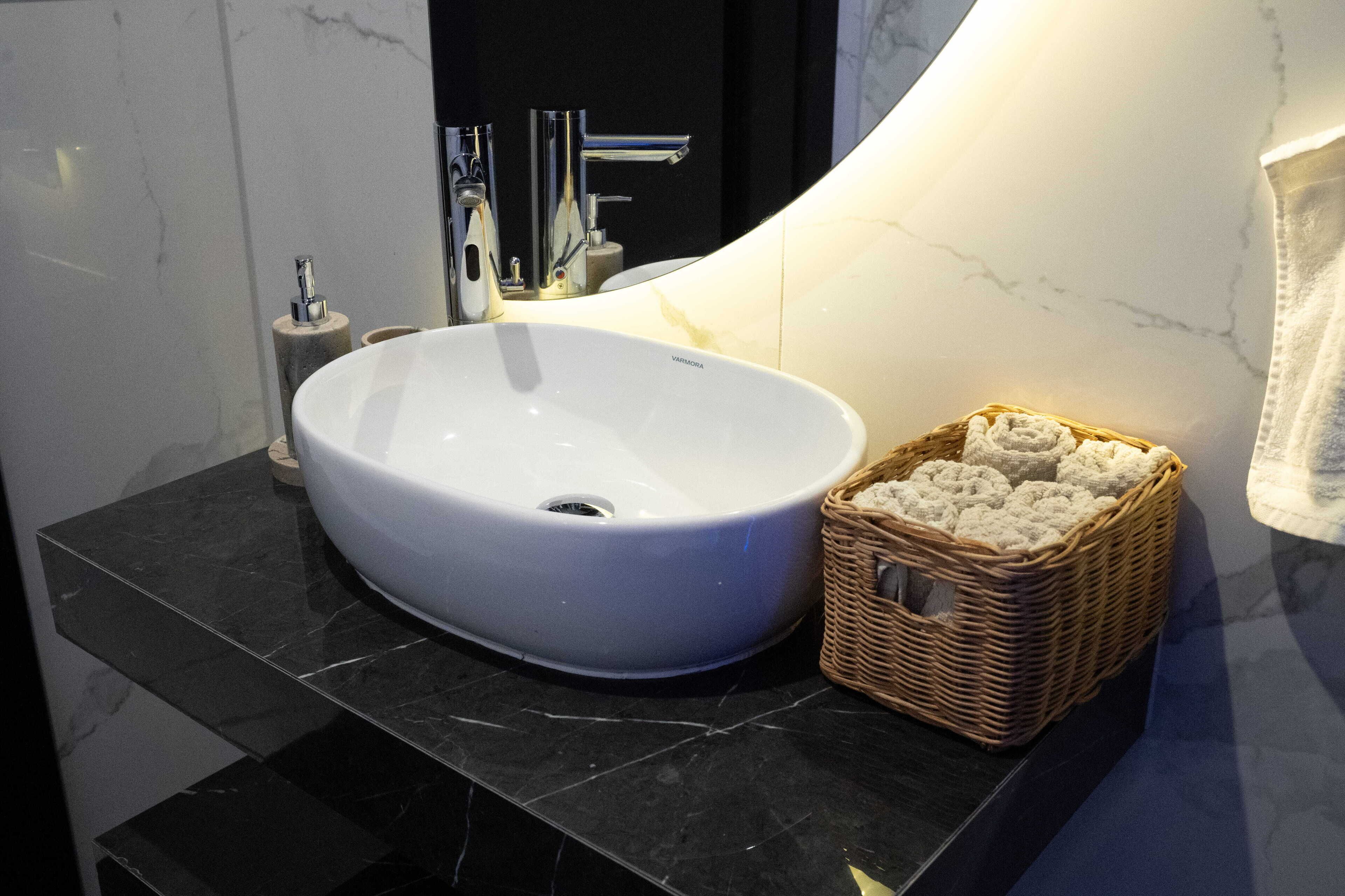 Ein Badezimmer mit einem weißen Waschtisch, einer schwarzen Marmorarbeitsplatte und einem Korbkörbchen mit Handtüchern.