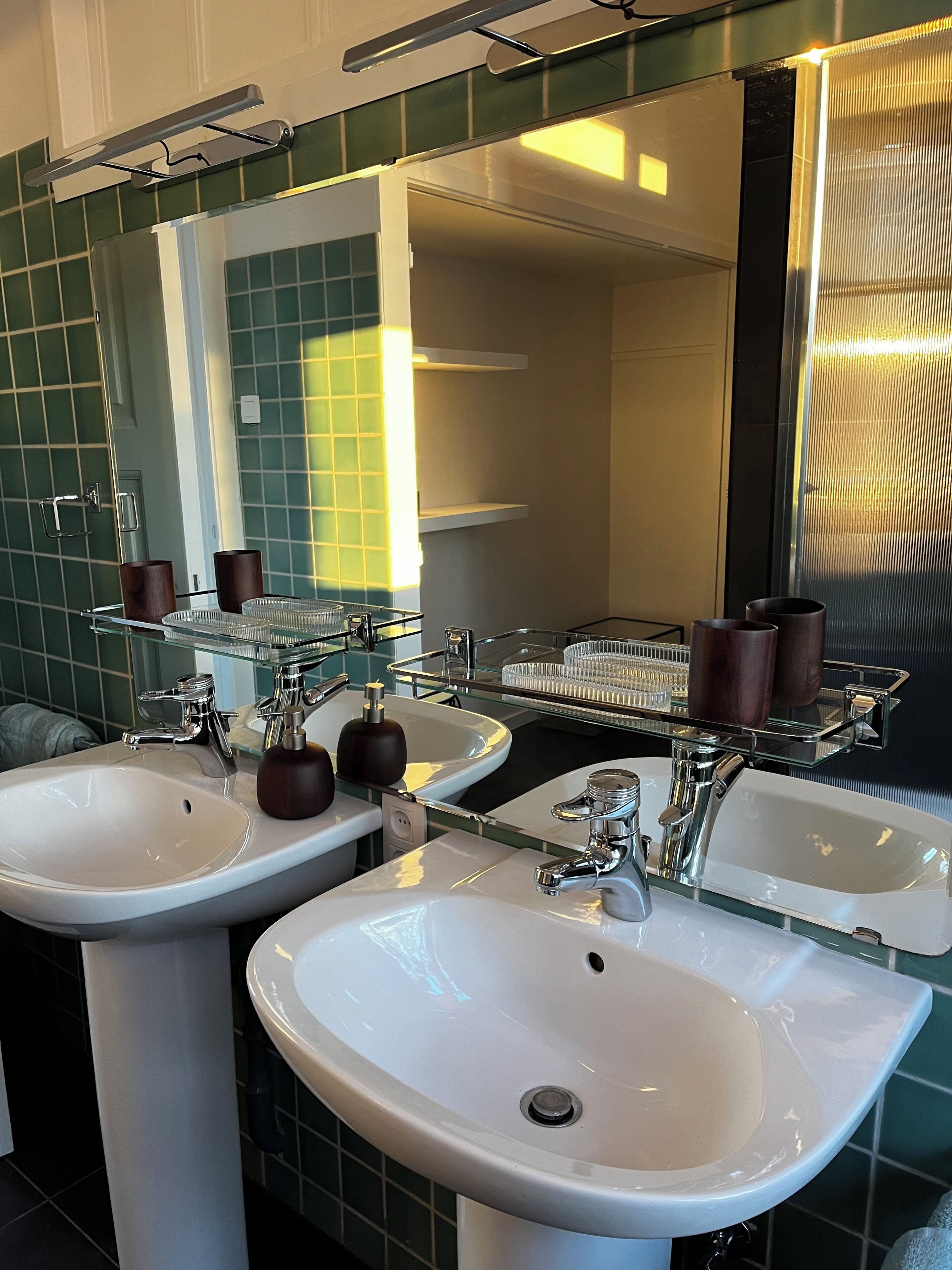 Un bagno con due lavandini, uno specchio e un ripiano in vetro con articoli da toilette.