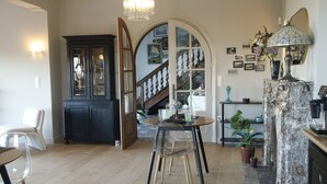 A dining area with a round table, chairs, a chandelier, a cabinet, and a staircase leading to another room. - Aux étangs fleuris (Rochefort)