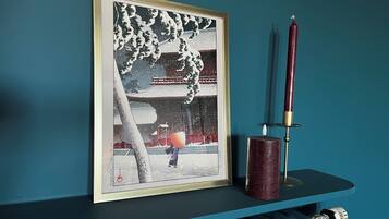 A framed artwork of a snowy scene with a person in traditional attire, a red candle, and a radiator below.