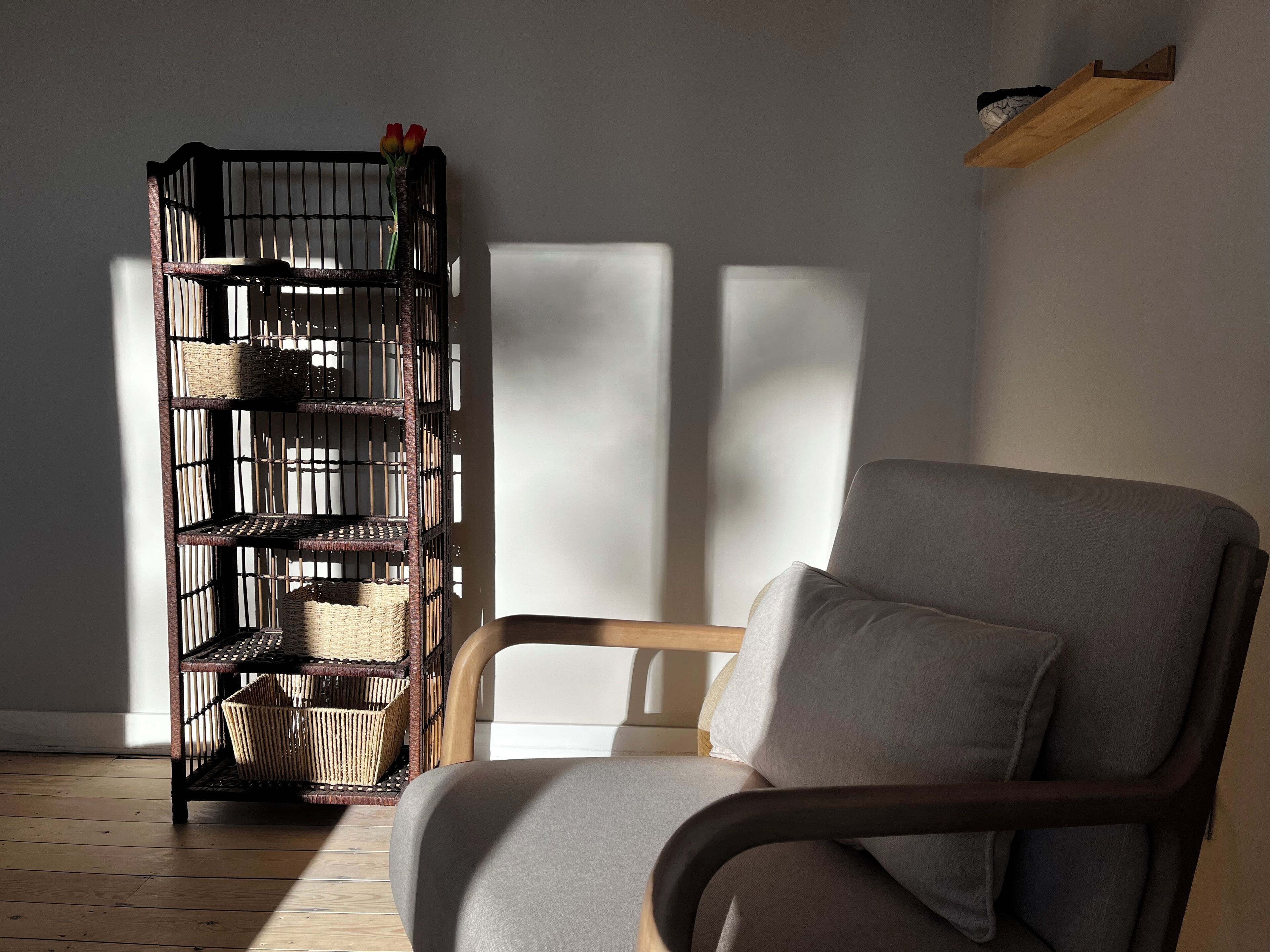 Ein Zimmer mit einem grau gepolsterten Sessel und einem Korbschrank an der Wand.