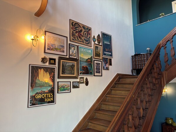 A staircase with wooden railings and a wall decorated with various framed artworks. - Aux étangs fleuris (Rochefort)