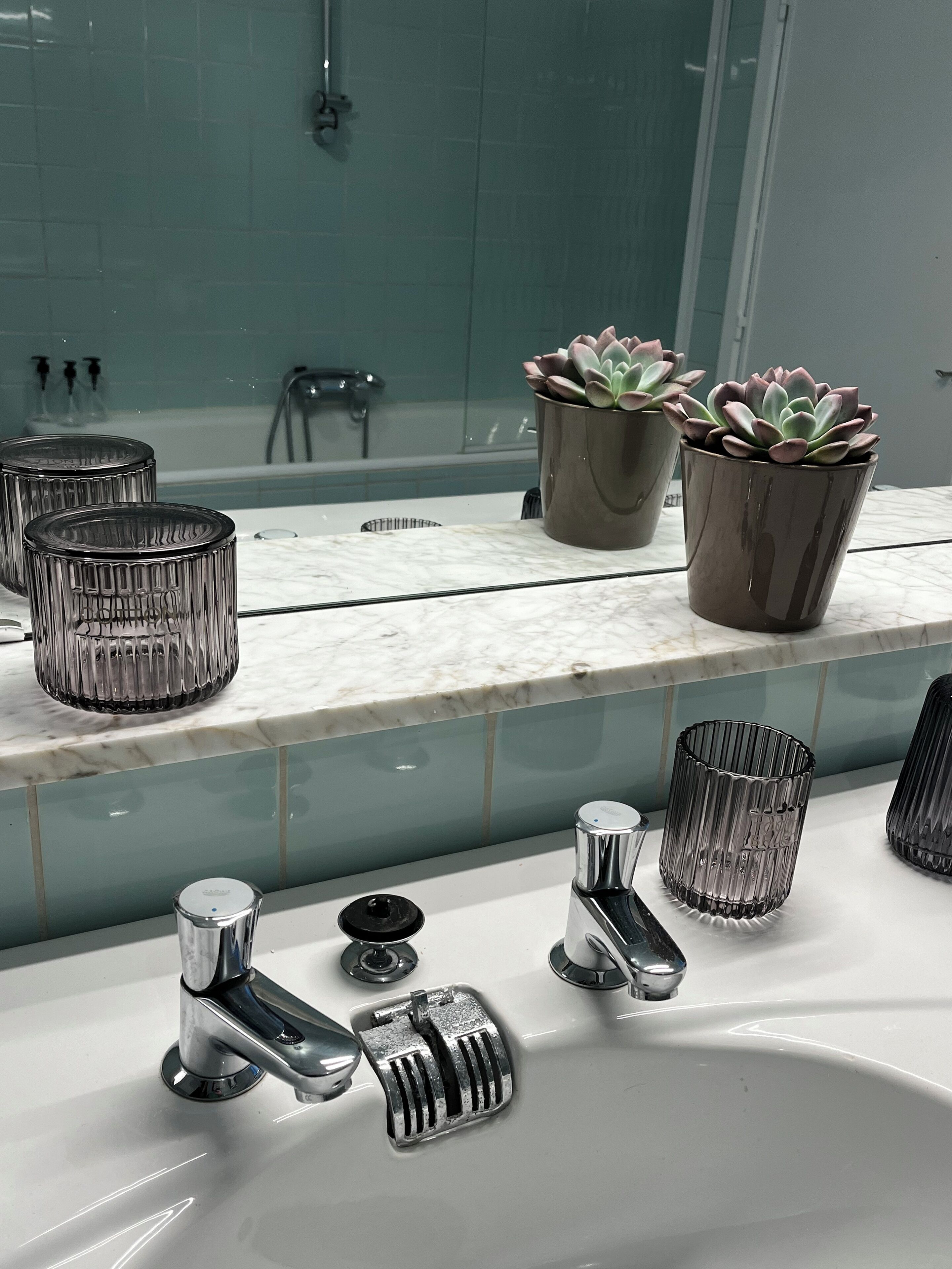 Un baño con encimera de mármol, dos lavabos y un espejo que refleja una bañera.