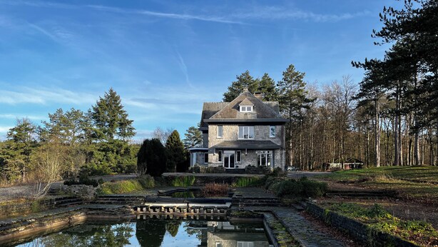 A stone house with a pond in front, surrounded by trees and a clear sky. - Aux étangs fleuris (Rochefort)