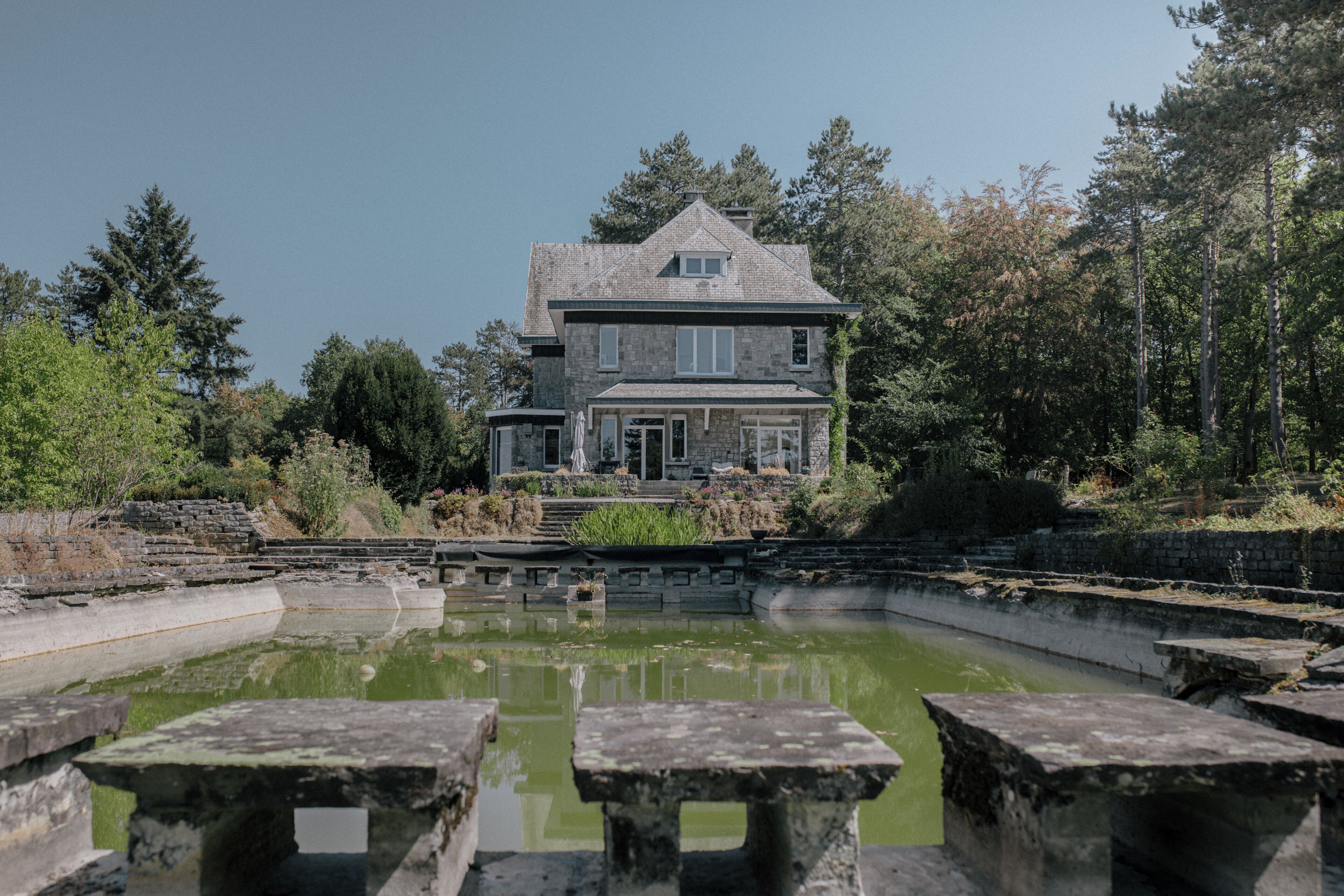 Un bâtiment en pierre avec un grand étang devant, entouré d’arbres.