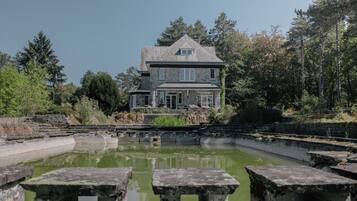 Un bâtiment en pierre avec un grand étang devant, entouré d’arbres.