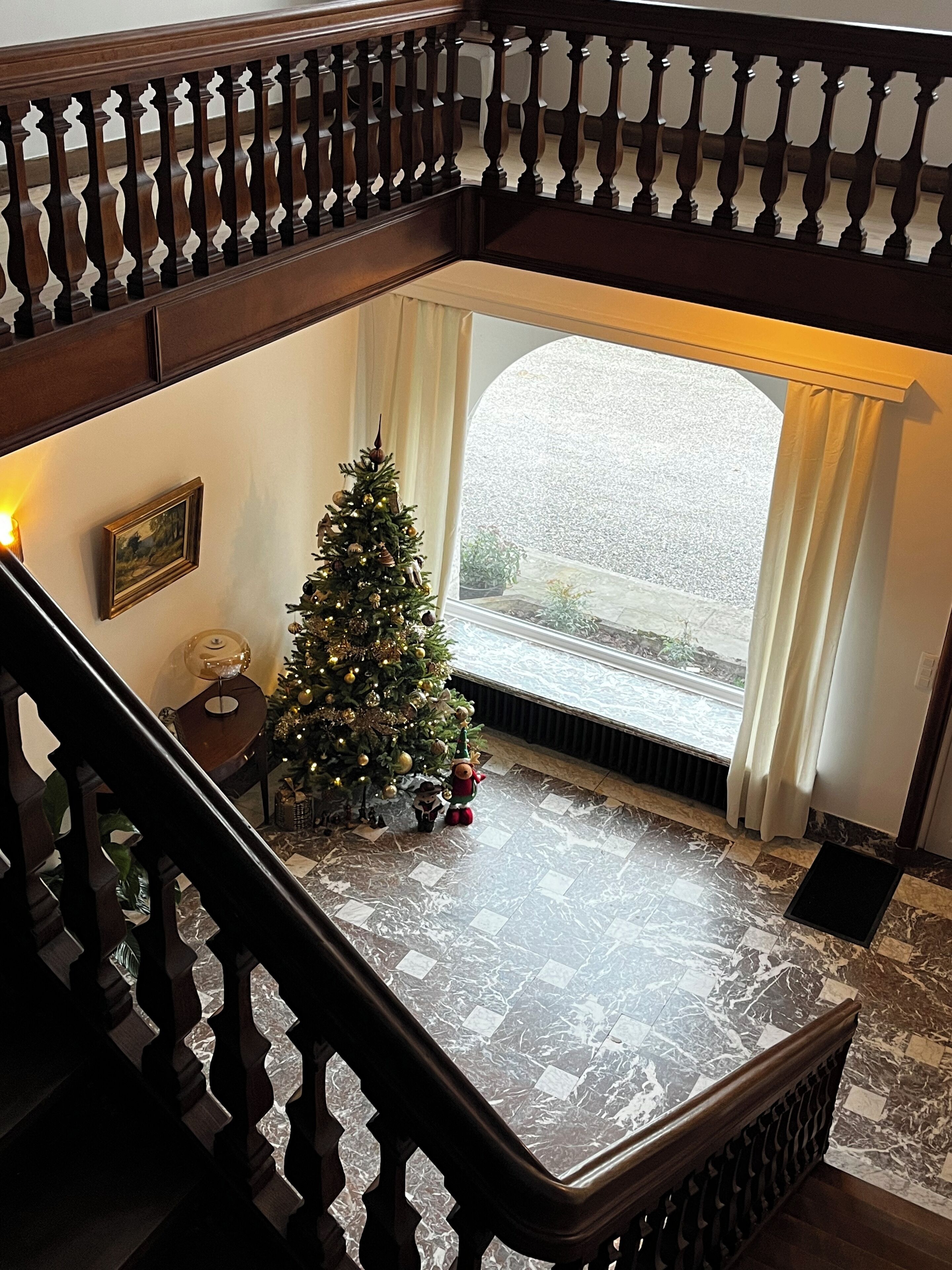 A staircase with a wooden railing leading to a balcony. A Christmas tree is decorated with ornaments and lights.