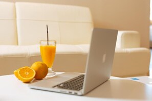 Una laptop sobre una mesa blanca, con un vaso de jugo de naranja y media naranja.