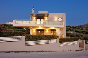 Una casa moderna de dues plantes amb un balcó, una xemeneia i un vestíbul ben il·luminat.