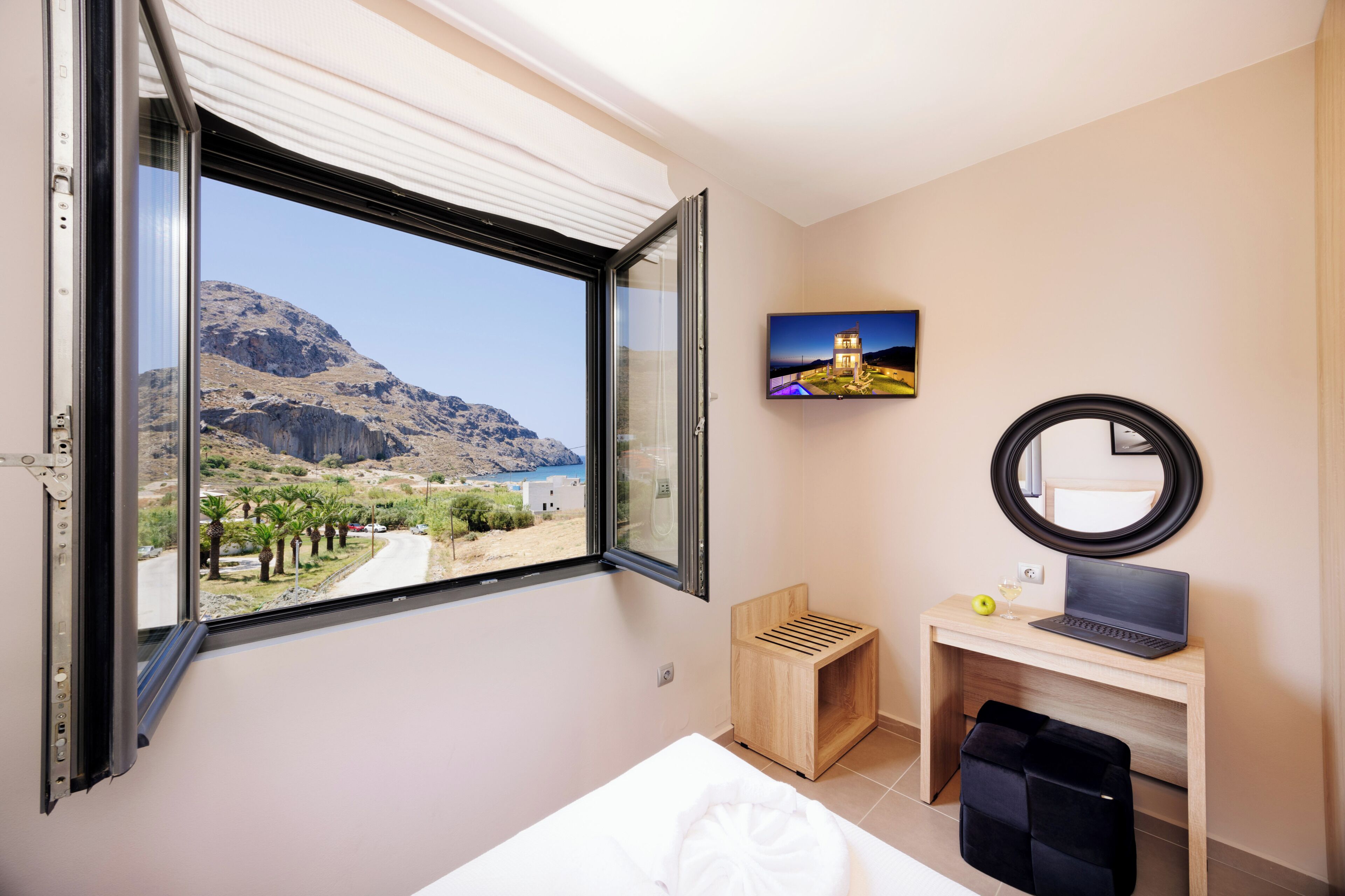 Habitación de hotel con un ventanal grande, un escritorio con una computadora portátil, un espejo y un cuadro en la pared.